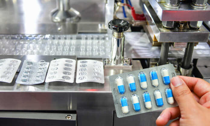 hand holding blue capsule pack medicine pill production line industrial pharmaceutical concept 1 696x464 1 e1652243060386